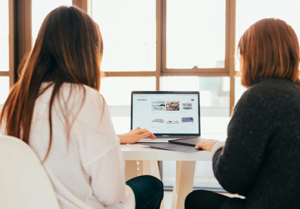 Two women looking over a retail catalogue on a MacBook pro