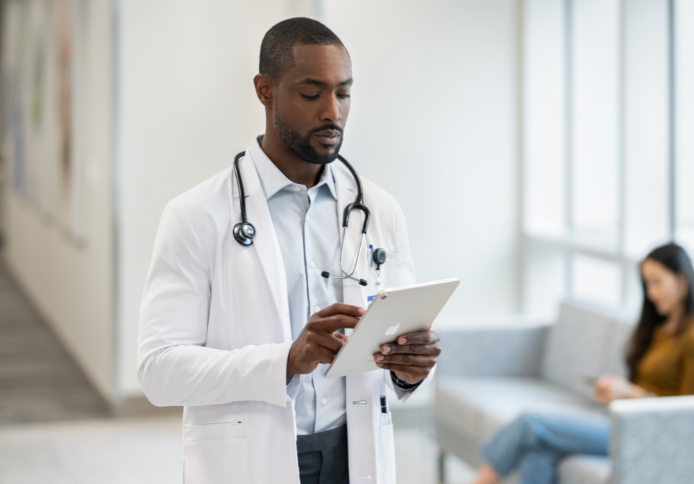 Physician using iPad while standing in the patient room<br />
