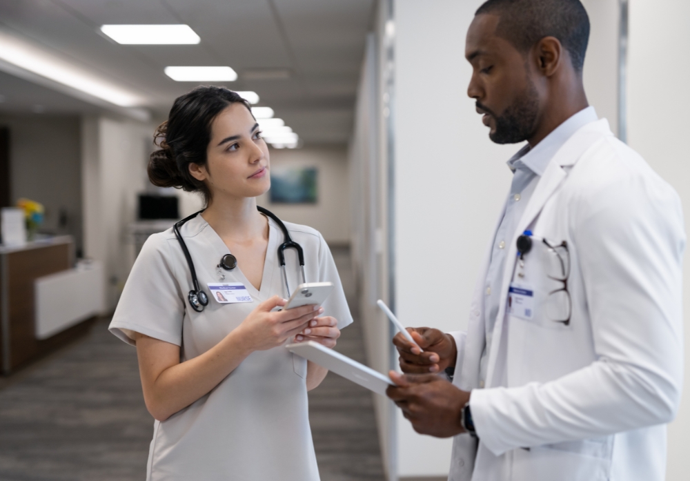 Nurse holding an iPhone while meeting with a doctor holding an iPad in the hallway